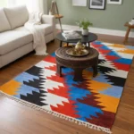 Colorful handwoven shataranji rug on wooden floor in a cozy living room with sofa, coffee table and decorative tea set | উডেন ফ্লোরের ওপর বিছানো রঙিন হাতে বোনা শতরঞ্জি রাগ, পাশে সোফা, কফি টেবিল ও ডেকোরেটিভ টি-সেটসহ একটি স্টাইলিশ লিভিং রুম